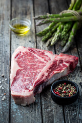 Raw T-bone Steak with fresh herbs and oil on dark wooden background
