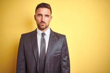 Young handsome business man over yellow isolated background skeptic and nervous, frowning upset...
