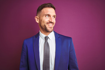 Young handsome business man over purple isolated background looking away to side with smile on face, natural expression. Laughing confident.