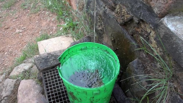 mountain landscape with water tap and green bucket