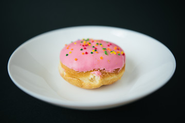 Pink round donut on white plate on black background