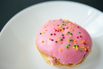 Pink round donut on white plate on black background