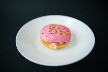 Pink round donut on white plate on black background