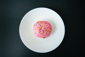 Pink round donut on white plate on black background
