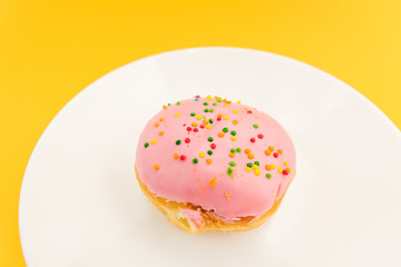 Pink round donut on white plate on yellow  background