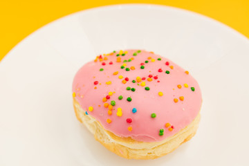 Pink round donut on white plate on yellow  background