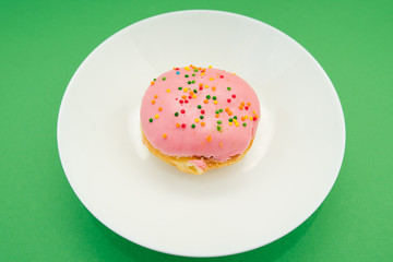 Pink round donut on white plate on green background