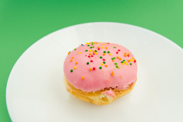 Pink round donut on white plate on green background