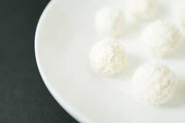 Chocolate covered coconut candies on white plate isolated on black background. Truffle candy set. Selective focus
