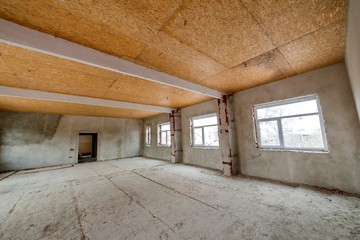 Unfinished apartment or house big loft room under reconstruction. Plywood ceiling, plastered walls, window openings, cement floor. Construction and renovation concept.