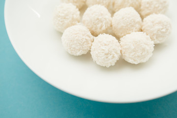 Chocolate covered coconut candies on white plate isolated on blue background. Truffle candy set. Selective focus