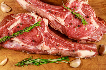 Raw fresh beef rib eye steak on bone with spices, garlic and rosemary on wooden table. Top view