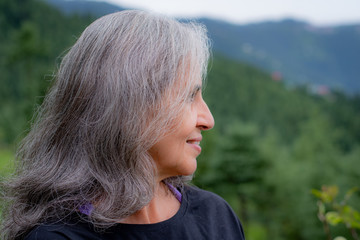 Graceful Indian ethnicity woman with gray hair standing in sports clothing against a scenic hilly backdrop.