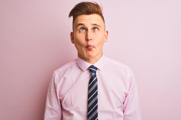 Young handsome businessman wearing shirt and tie standing over isolated pink background making fish face with lips, crazy and comical gesture. Funny expression.