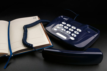 Outdated push-button telephone with handset and personal organizer on black background