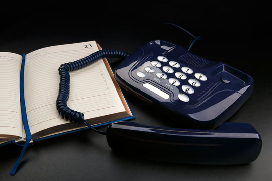 Outdated push-button telephone with handset and personal organizer on black background