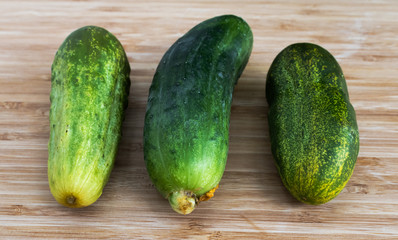 Three green cucumbers of different shades on a light brown background, close-up