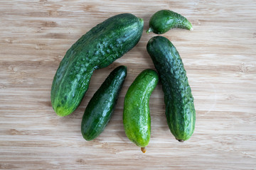 Five green ugly cucumbers lie on a light brown wooden surface, top view