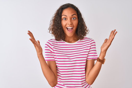 Young brazilian woman wearing pink striped t-shirt standing over isolated white background celebrating crazy and amazed for success with arms raised and open eyes screaming excited. Winner concept