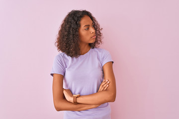 Young brazilian woman wearing t-shirt standing over isolated pink background looking to the side with arms crossed convinced and confident