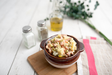 Bowl of traditional Russian salad called Olivie, Russian New Year or Christmas salad on wooden background. Salad from cooked vegetables. Potato salad. 