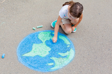 the  child girl draws a planet of the world with colored chalk on the asphalt. Children's drawings, paintings and concepts. Education and art, be creative when you return to school.  earth, Peace day