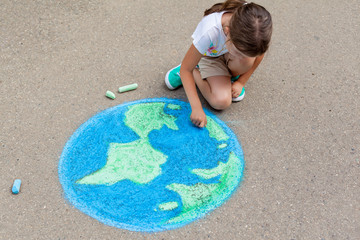 the  child girl draws a planet of the world with colored chalk on the asphalt. Children's drawings,...
