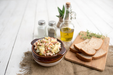 Bowl of traditional Russian salad called Olivie, Russian New Year or Christmas salad on wooden background. Salad from cooked vegetables. Potato salad. 