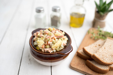 Olivie Salad. Bowl of traditional Russian salad called Olivie, Russian New Year or Christmas salad on wooden background. Salad from cooked vegetables. Potato salad. 