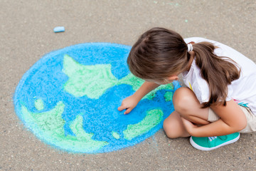 the  child girl draws a planet of the world with colored chalk on the asphalt. Children's drawings, paintings and concepts. Education and art, be creative when you return to school.  earth, Peace day