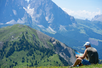 un homme assis dans l'herbe au dessus d'une montagne regarde une carte
