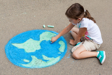 the  child girl draws a planet of the world with colored chalk on the asphalt. Children's drawings,...