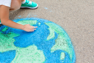 the  child girl draws a planet of the world with colored chalk on the asphalt. Children's drawings,...