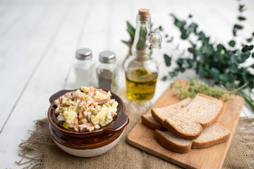 Bowl of traditional Russian salad called Olivie, Russian New Year or Christmas salad on wooden background. Salad from cooked vegetables. Potato salad. 