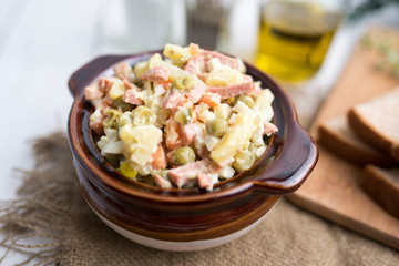 Bowl of traditional Russian salad called Olivie, Russian New Year or Christmas salad on wooden background. Salad from cooked vegetables. Potato salad. 
