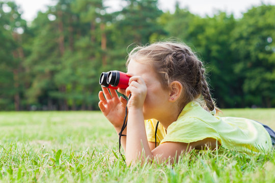 Funny child little girl looking through binoculars on sunny summer day.  Lifestyle, happy summertime, summer camp, Active family time on nature. Hiking with little kids. 