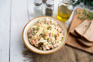 Bowl of traditional Russian salad called Olivie, Russian New Year or Christmas salad on wooden background. Salad from cooked vegetables. Potato salad. 