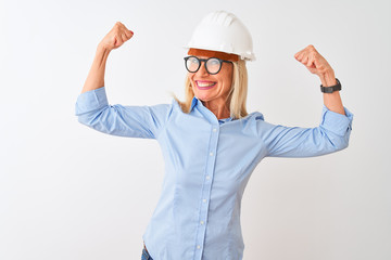 Middle age architect woman wearing glasses and helmet over isolated white background showing arms muscles smiling proud. Fitness concept.