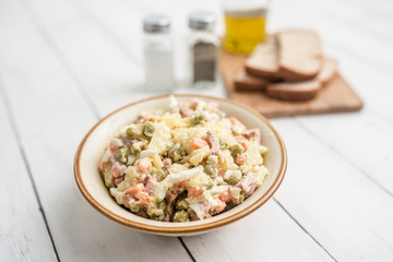 Bowl of traditional Russian salad called Olivie, Russian New Year or Christmas salad on wooden background. Salad from cooked vegetables. Potato salad. 