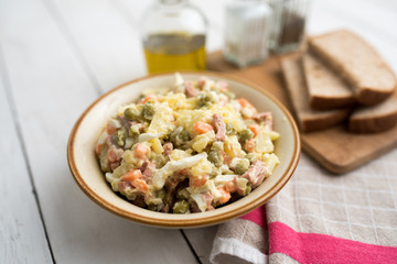 Bowl of traditional Russian salad called Olivie, Russian New Year or Christmas salad on wooden background. Salad from cooked vegetables. Potato salad. 