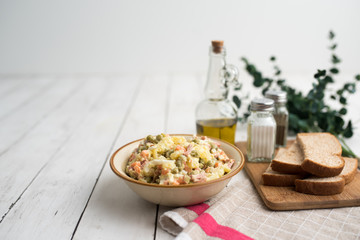Bowl of traditional Russian salad called Olivie, Russian New Year or Christmas salad on wooden background. Salad from cooked vegetables. Potato salad. 