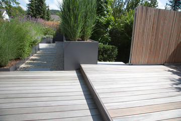 Moderne Garten- und Terrassengestaltung im Materialmix: Terrassen und Wand aus Holz , Gehweg aus Steinplatten umgeben von Schotter und mit Grünpflanzen bepflanzten Kübeln