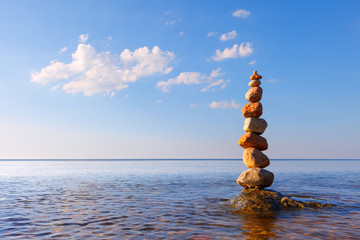 Rock zen pyramid of colorful pebbles standing in the water on the background of the sea