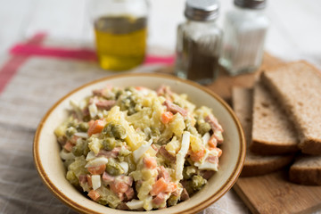 Bowl of traditional Russian salad called Olivie, Russian New Year or Christmas salad on wooden background. Salad from cooked vegetables. Potato salad. 