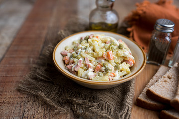 Bowl of traditional Russian salad called Olivie, Russian New Year or Christmas salad on wooden background. Salad from cooked vegetables. Potato salad. 