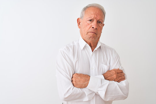 Senior grey-haired man wearing elegant shirt standing over isolated white background skeptic and nervous, disapproving expression on face with crossed arms. Negative person.