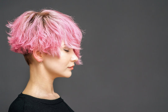 Studio shot of girl with nice pink hairdo, red lipstick on her lips, stands with closed eyes. Copy space