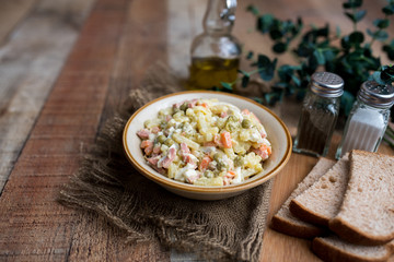 Bowl of traditional Russian salad called Olivie, Russian New Year or Christmas salad on wooden background. Salad from cooked vegetables. Potato salad. 