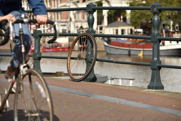 A lone wheel in Amsterdam, while cyclist passes by