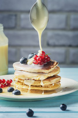 Pancakes are watered with condensed milk. Tasty breakfast with berries. Dessert with currants and blueberries close-up.